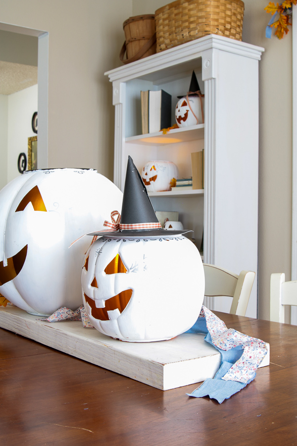 White painted jack-o'-lantern wearing a paper witch hat with gingham ribbon and fabric strips