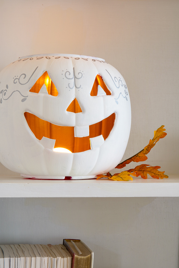 White chalk painted jack-o'-lantern glowing with a battery light on a bookshelf