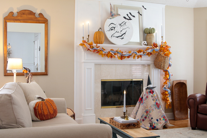 Cozy cottage living room decorated for Halloween with a vintage quilt ghost, moon face mantel, and pumpkin pillow