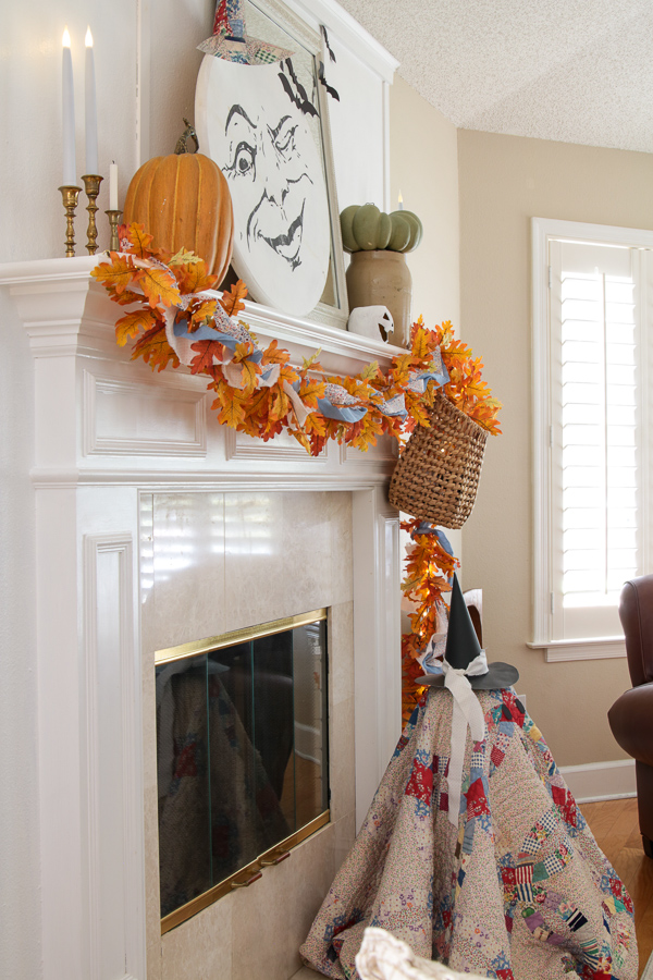 Side view of a Halloween mantel with a moon face, faux pumpkins, hanging basket, and a quilt ghost below