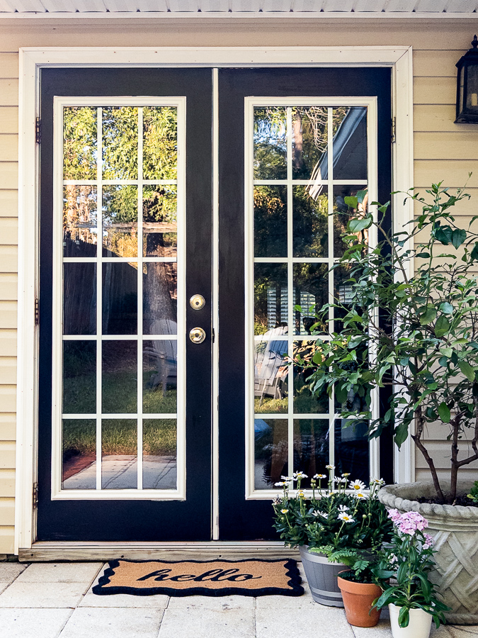 Front view of black French patio doors with white trim and a lantern sconce on a cream-sided house