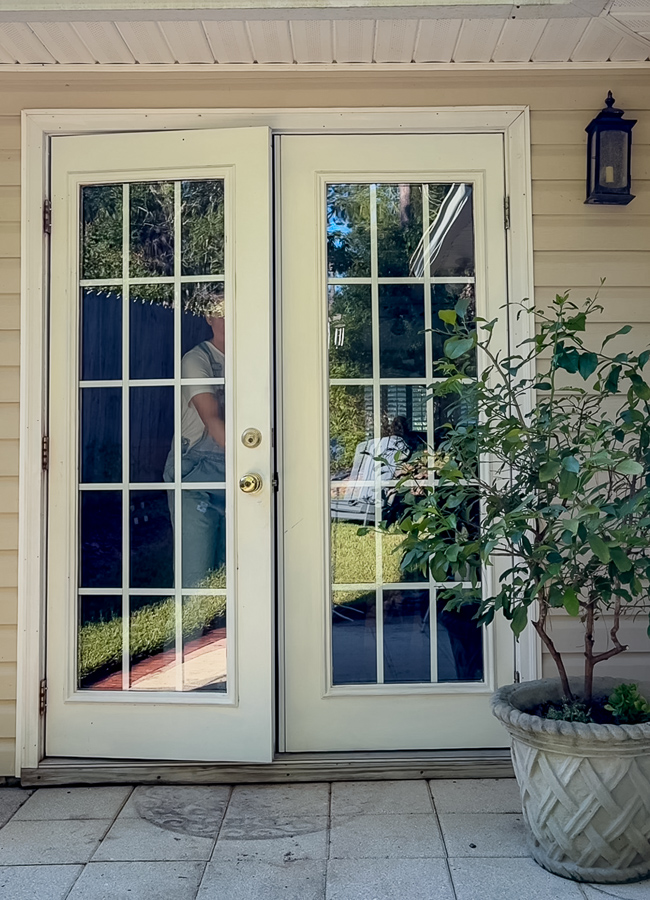 Before photo of white French patio doors with glass panes, white trim, and a potted orange tree on the patio
