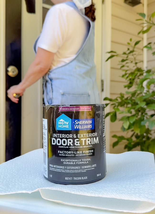 Quart of Tricorn Black door and trim paint on a paper towel on a stool while painting French patio doors black