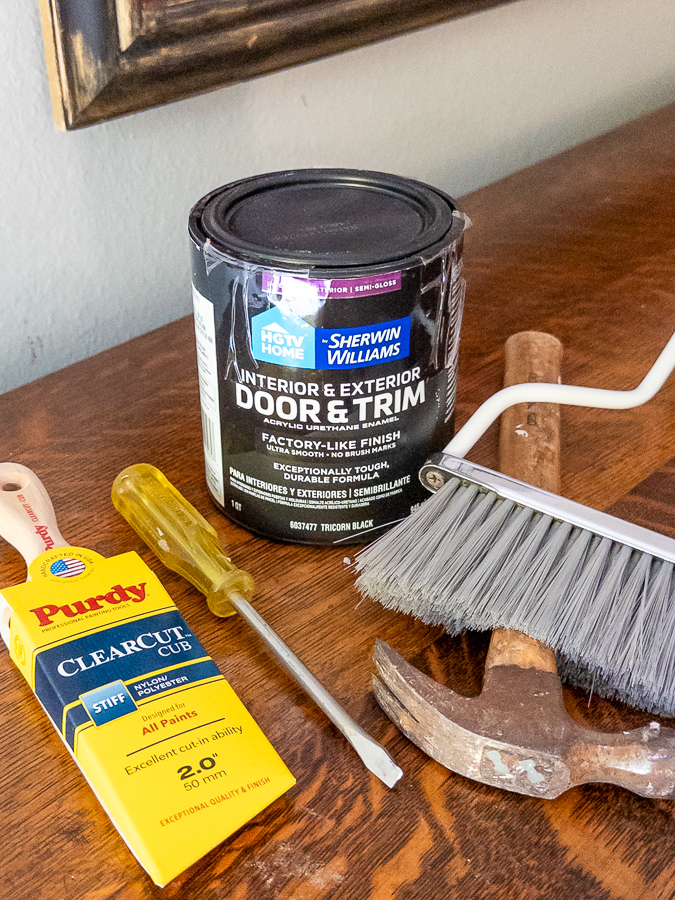 Supplies for painting patio doors black: HGTV Home by Sherwin-Williams Door and Trim paint in Tricorn Black, a Purdy Clearcut Cub angled brush, a screwdriver, a hammer, and a hand broom