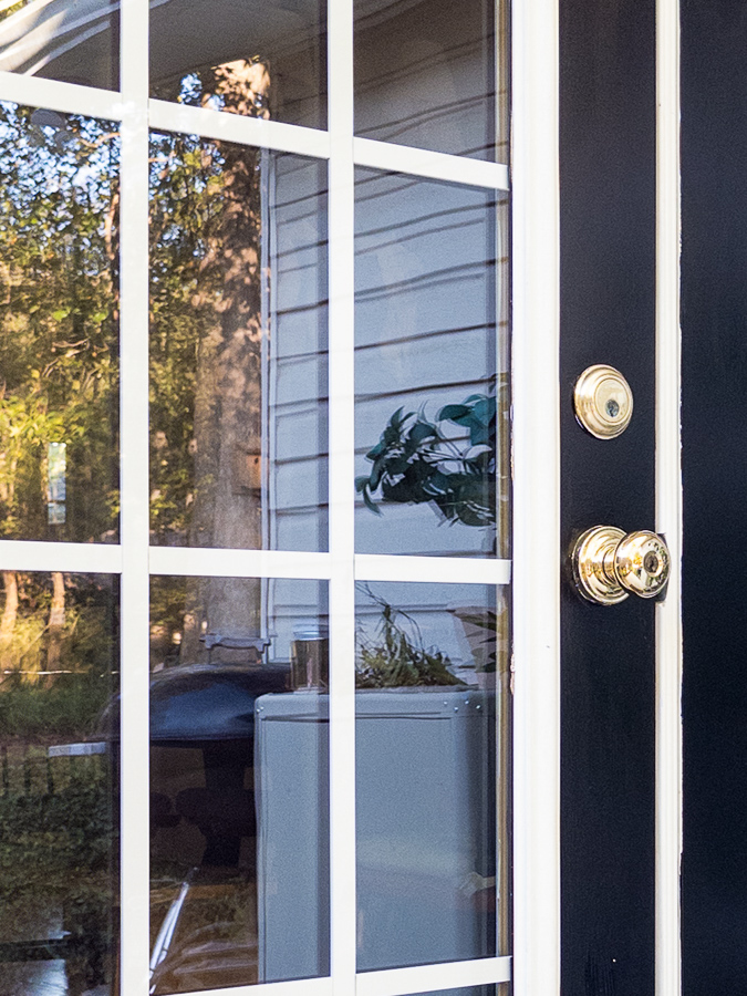 Close-up of black French doors with white trim, white mullions, and brass door hardware